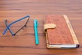 Brown business diary with ball pen and specks lying on wooden table Royalty Free Stock Photo