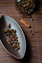 Brown canoe-shaped dish on bamboo mat with coffee beans, star anise, cloves and cinnamon