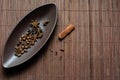 Brown canoe-shaped dish on bamboo mat with coffee beans, star anise, cloves and cinnamon