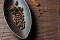 Brown canoe-shaped dish on bamboo mat with coffee beans, star anise, cloves and cinnamon