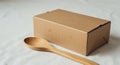 A brown cardboard box rests on a white surface next to a wooden spoon with a Royalty Free Stock Photo