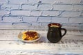 A brown ceramic cup with hot tea and a plate of waffles with strawberry jam