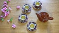 Brown ceramic teapot and teacups arranged on wooden table with bouquet decoration, top view of tea set