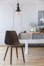 Brown chair under lamp in white dining room interior with table and wall with molding. Real photo Royalty Free Stock Photo