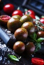 Brown cherry tomatoes with sea salt and green basil on dark table, autumn harvest, selective focus Royalty Free Stock Photo