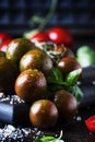 Brown cherry tomatoes with sea salt and green basil on dark table, autumn harvest, selective focus Royalty Free Stock Photo