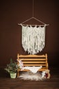 Brown chocolate interior area for photographing babies, wooden bench with white carpet, macrame light tapestry on the wall