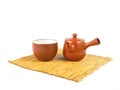 Brown clay teapot and cup on a bamboo mat isolated on a white background. Royalty Free Stock Photo