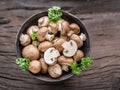 Brown colored common mushrooms in wooden bowl on wooden table with herbs. Top view