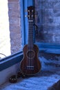 Brown colored ukulele with strap leaning against a brick window frame. Concept instruments, music, strings Royalty Free Stock Photo