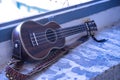 Brown colored ukulele with strap leaning against a brick window frame. Concept instruments, music, strings Royalty Free Stock Photo