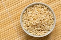 Brown cooked rice in a white ceramic bowl isolated on bamboo matt from above. Space for text Royalty Free Stock Photo