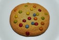 A brown cookie with colorful milk chocolate candies on white isolated background