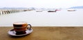 Brown cup of coffee on concrete table with seascape, ocean, bridge and boat background.