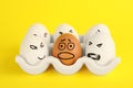 Brown egg with scared face among aggressively depicted white ones in holder on yellow background. Stop racism