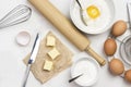 Brown eggs on metal stand. Butter and knife on paper. Egg yolk with flour and spoon in bowl. Milk in bowl and rolling pin on table Royalty Free Stock Photo