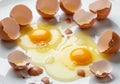 Brown eggshells, cracked into several pieces, are scattered on a white surface with two raw egg Royalty Free Stock Photo