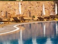 Brown empty loungers near the swimming pool with blue water and closed umbrellas early in the morning Royalty Free Stock Photo