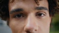 Brown eyes man looking camera outdoors extreme closeup. Curly teen staring lens