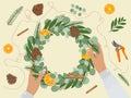 Brown female hands hold and make Christmas wreath with eco-friendly materials. Fir, pine cone, cinnamon, dry orange, secateurs.