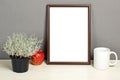 Brown frame mockup with plant pot, mug and apple on wooden shelf Royalty Free Stock Photo