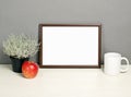 Brown frame mockup with plant pot, mug and apple on wooden shelf Royalty Free Stock Photo