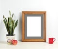 Brown frame mockup with plant pot, mug and apple on wooden shelf Royalty Free Stock Photo