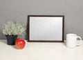 Brown frame mockup with plant pot, mug and apple on wooden shelf Royalty Free Stock Photo