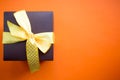 Brown gift box with yellow ribbon on orange background. Top view with copy space. Royalty Free Stock Photo