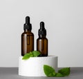 Brown glass bottles with herbal oil and green mint leaves on product stage gray background Royalty Free Stock Photo