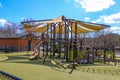 A brown and green jungle gym in the park with a yellow trap roof surrounded by green Astroturf, buildings, parked cars Royalty Free Stock Photo