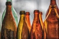 Brown and green old glass bottles on windowsill, with curtain. Closeup, daylight