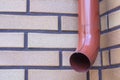 Brown gutter pipe against a brick wall background