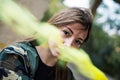 Brown hair girl holds a smoke bomb that throws yellow smoke around. Young girl wears an urban style, military jacket and piercing