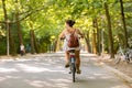 A brown hair woman with a brown leather backpack cycling in the Amsterdam Vondelpark on a summerday