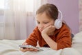 Brown haired little girl in children\'s room with headphones and smartphone using mobile phone with headset and watching Royalty Free Stock Photo