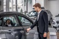 Brown-haired male opening car door in the showroon