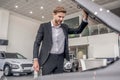 Brown-haired male opening car hood in showroom