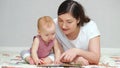 Brown-haired mother reads book to amused baby girl on floor