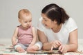 Brown-haired mother reads book to amused baby girl on floor