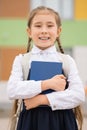 Brown-haired schoolgirl holding book enjoys attending school