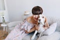 Brown-haired smiling girl in pink dress playing with her cute beagle dog at home. Indoor portrait of lovely young lady Royalty Free Stock Photo