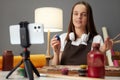 Brown haired woman wearing brown apron painting using mobile phone on tripod at her workplace broadcasting online master class Royalty Free Stock Photo