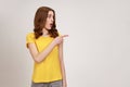 Brown haired woman of young age in yellow casual T-shirt pointing away looking with big eyes and Royalty Free Stock Photo