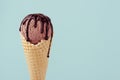 Brown ice cream in waffle cone with chocolate sauce on soft light pastel green background, closeup, half, details.