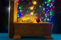 Brown jewelry box with shiny gold New Year/Christmas decoration is on the blue table. There are different colors lights. Royalty Free Stock Photo
