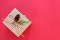 Brown kraft gift box tied with twine and decorated with a cone and a branch of an evergreen bush on a dark burgundy background