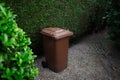 Brown large plastic bin for trash on backyard, around of tree hedge