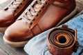 Brown leather men`s boots, belt and blue jeans on a dark wooden background, close up Royalty Free Stock Photo