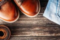 Brown leather men`s boots, belt and blue jeans on a dark wooden background, top view with copy space Royalty Free Stock Photo